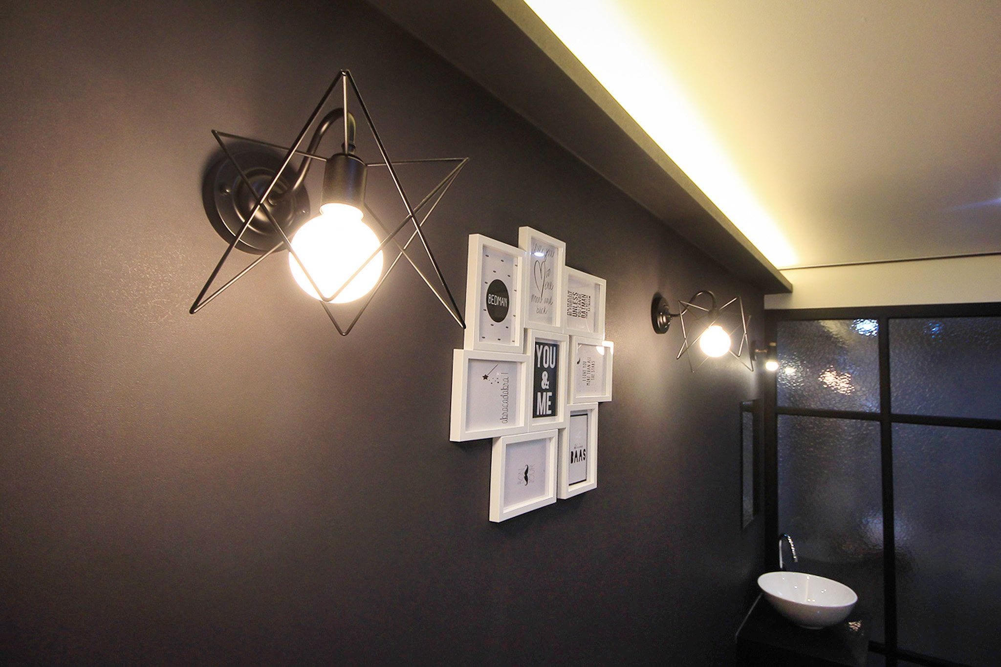 Ein modernes Badezimmer mit einer sternförmigen Leuchte, gerahmten Bildern an der Wand und einem weißen Waschbecken.