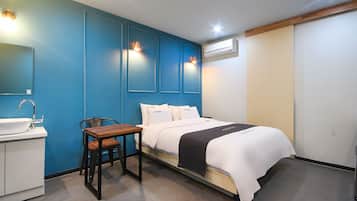 A hotel room with a bed, bedside table, chair, and a small desk with a sink.