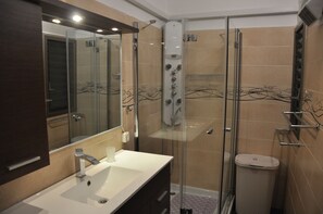 A modern bathroom with a glass-enclosed shower, a large mirror, and a white sink.