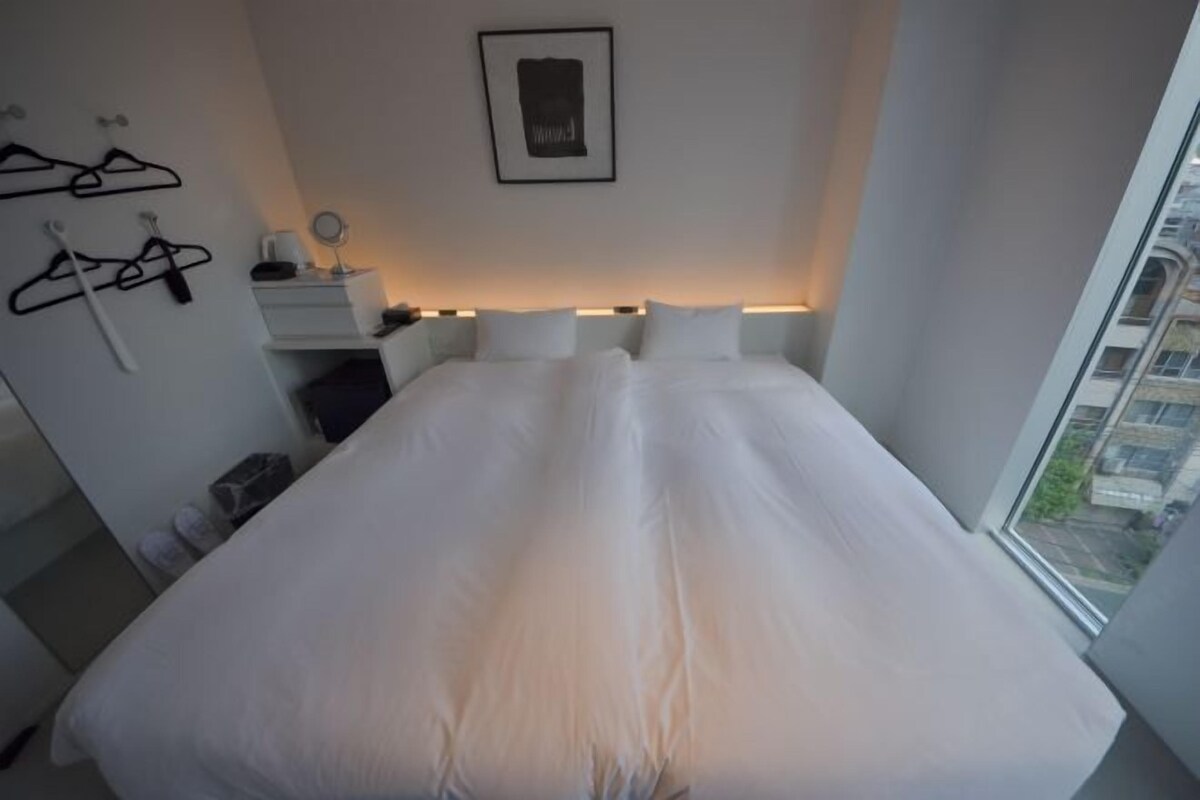 A modern bedroom with a large bed, bedside tables, a hanging coat rack, and a framed picture on the wall.