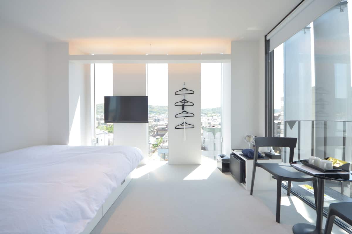 Une chambre d’hôtel moderne dotée d’un grand lit, d’un bureau avec une chaise, d’une télévision et offrant une vue sur la ville grâce à de grandes fenêtres.