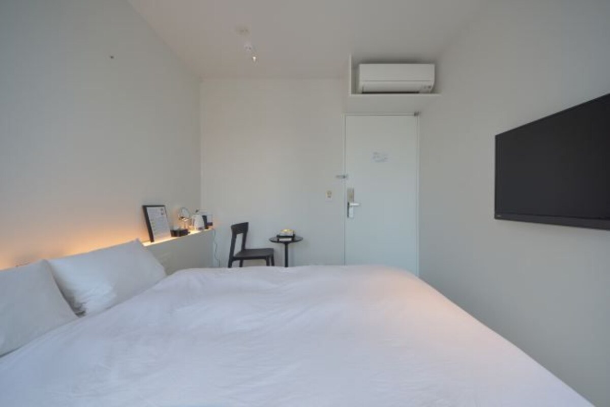 Una camera d'albergo con un letto, una sedia, un tavolino e una TV a parete.