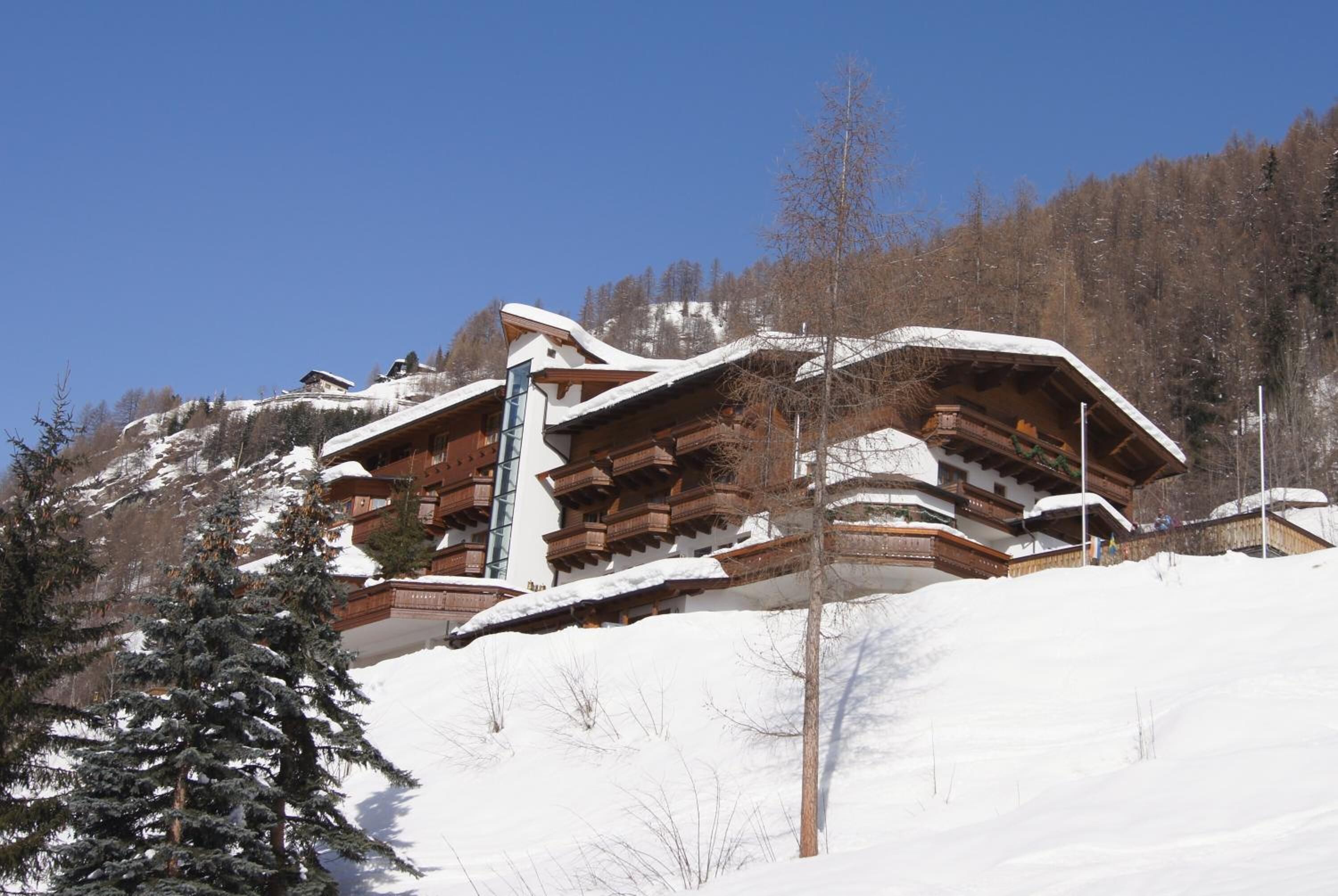 Un edificio de estilo chalet con techo pronunciado, balcones de madera y un telesilla visible al fondo.