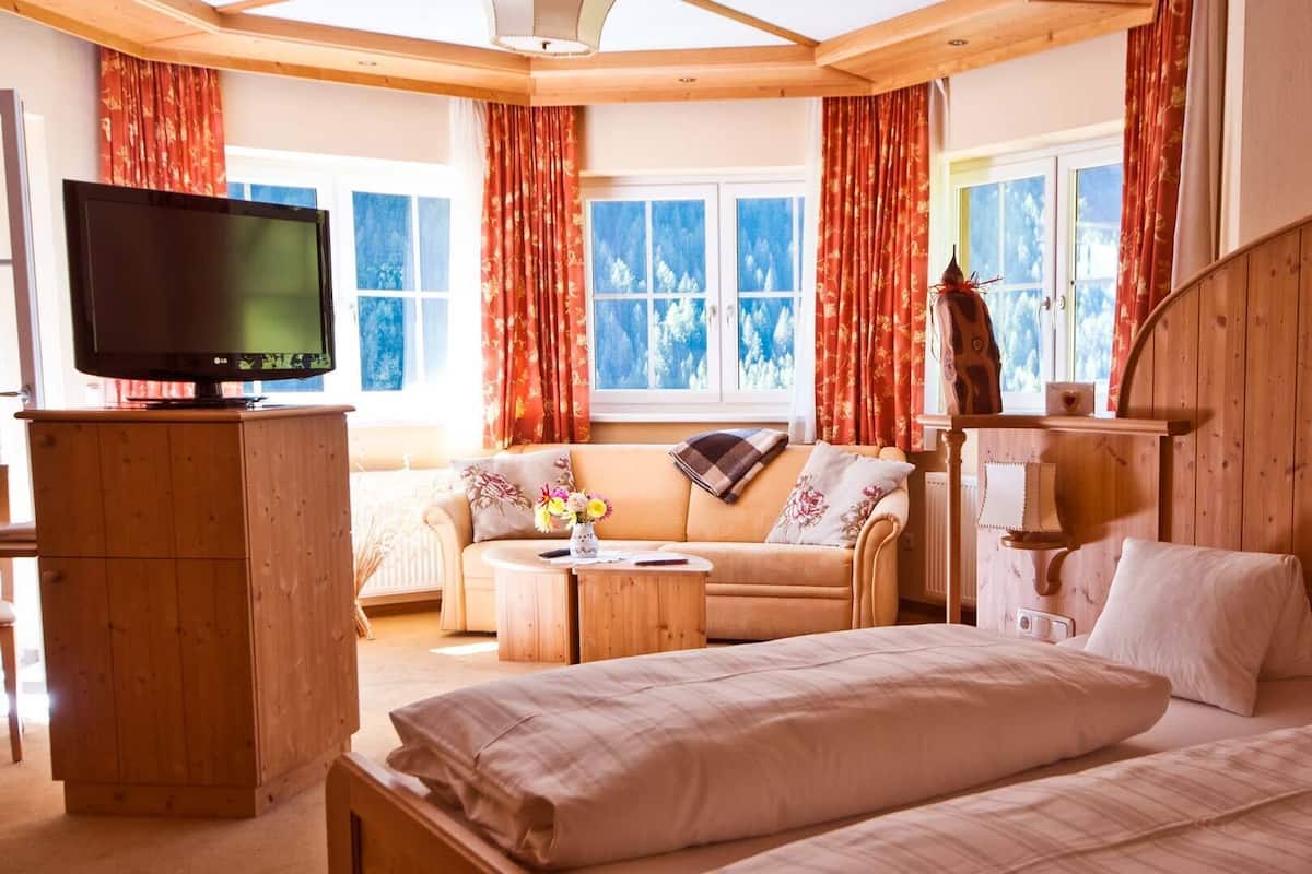 Ein gemütliches Hotelzimmer mit einem großen Bett, einer Couch, einem Fernseher und einem Holzschrank.