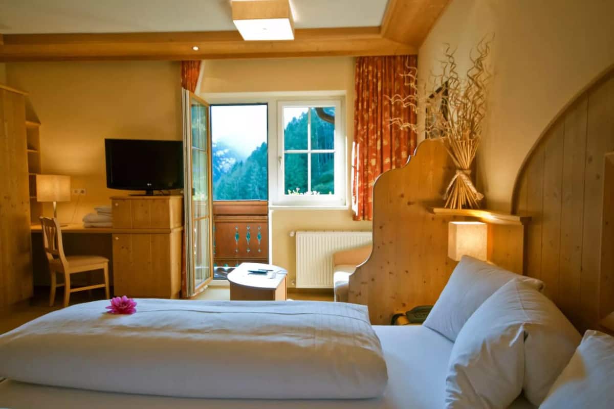 Ein Hotelzimmer mit Bett, Schreibtisch, Fernseher und Blick auf Berge durch ein Fenster.