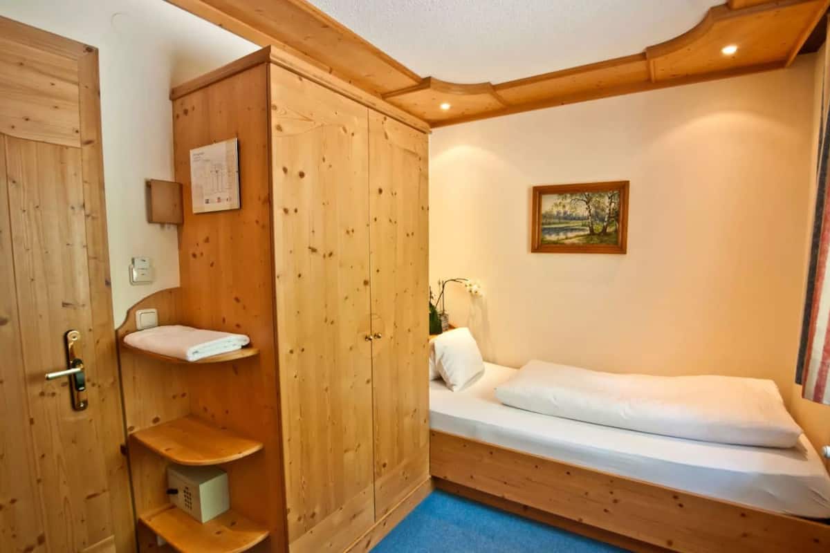 Ein kleines, gemütliches Zimmer mit einem Holzschrank, einem Einzelbett und einem kleinen Regal.