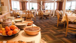 Un bufé de desayuno con frutas, pasteles y café en un comedor bien iluminado con varias mesas y sillas.