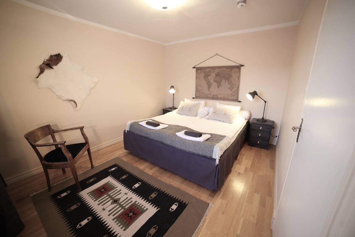Un dormitorio con una cama, una silla, un tapete, un mapa en la pared y una mesita de noche con una lámpara.