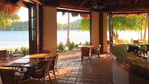 Un restaurant offrant une vue sur un lac, doté d’une terrasse et d’un toit de chaume.