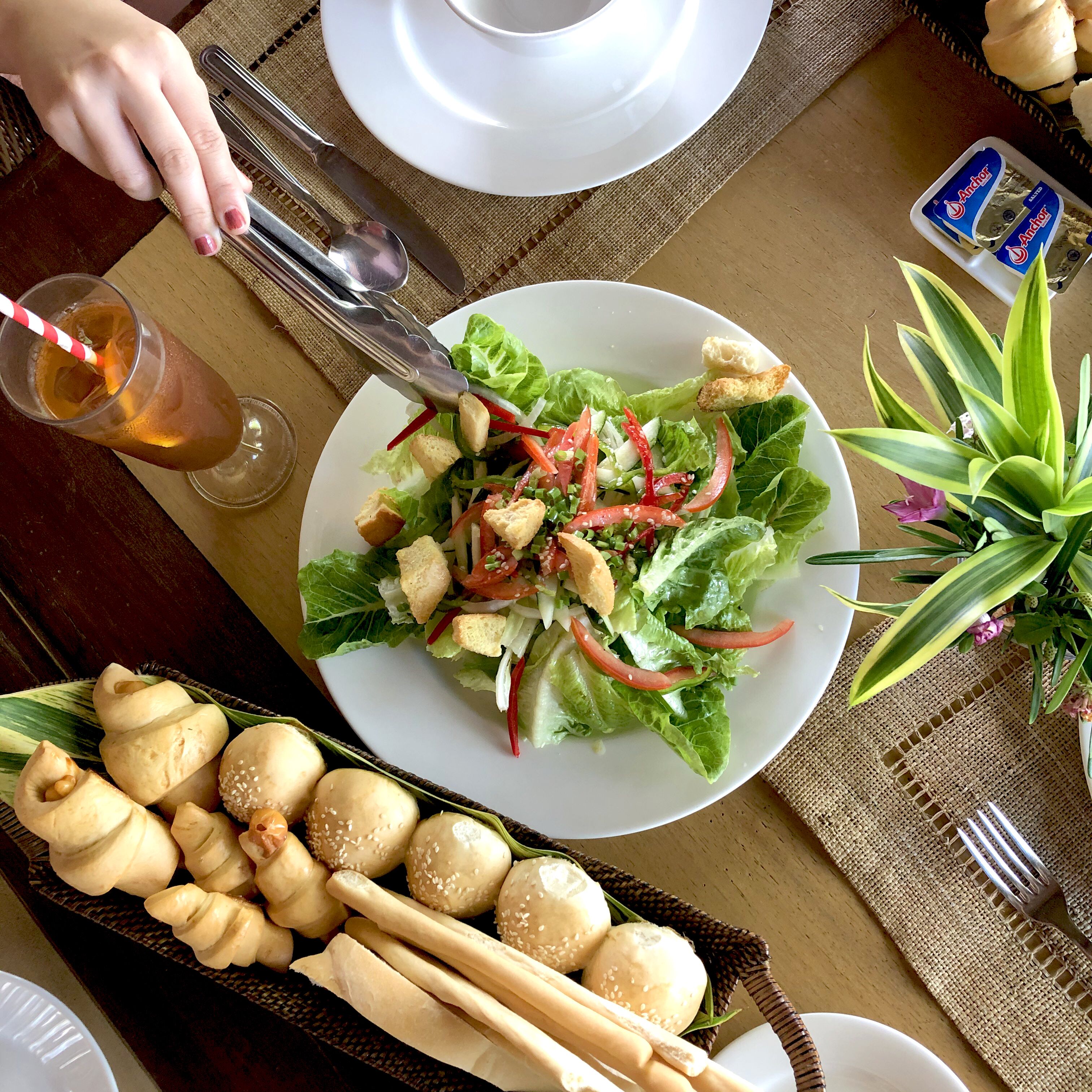 A dining table with a plate of salad, bread, and a drink.