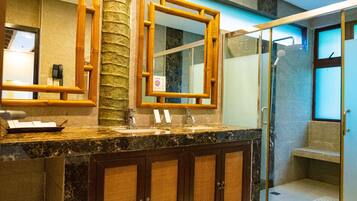 Un bagno con piano in marmo, mobiletti in legno, uno specchio con cornice in legno e box doccia in vetro.