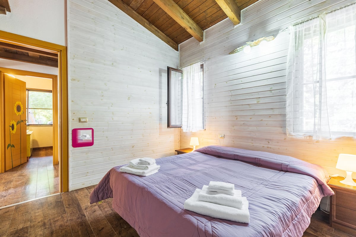 A room with wooden walls, a bed with purple bedding, and a wooden door with a sunflower decoration.