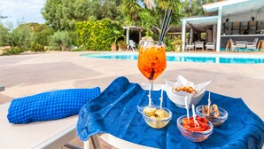 A poolside setting with a blue towel, a glass of iced drink, and two small bowls of food on a table.