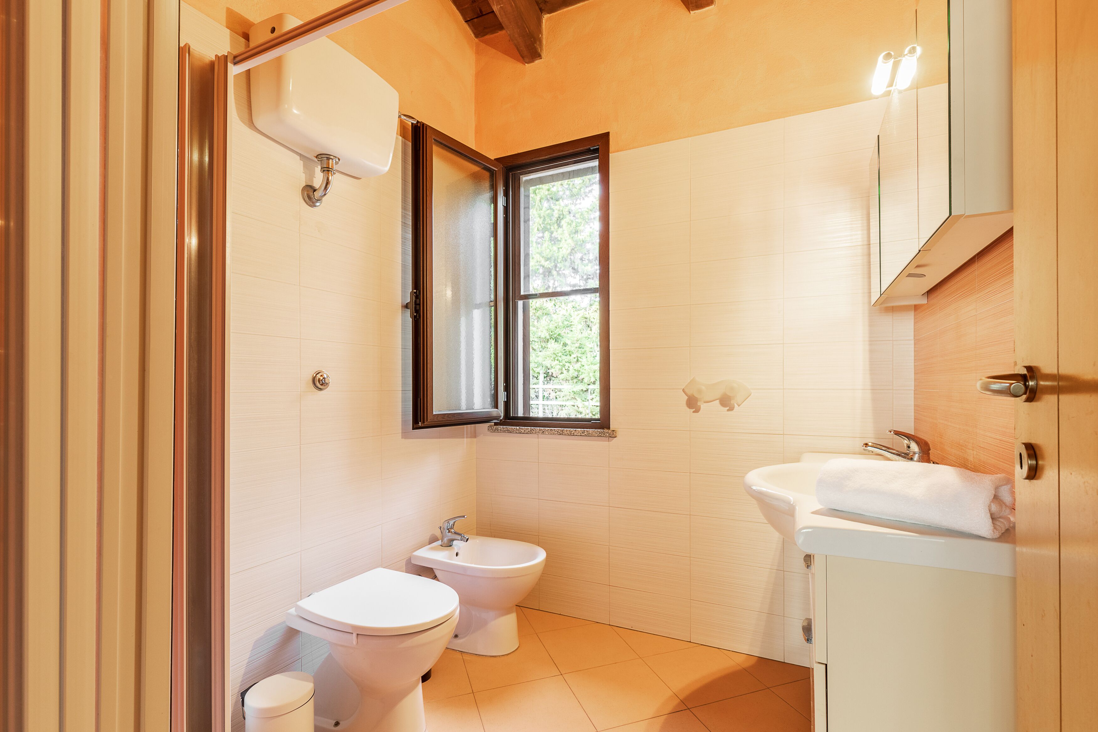Un bagno con servizi igienici, bidet e lavabo, una finestra e travi in legno al soffitto.