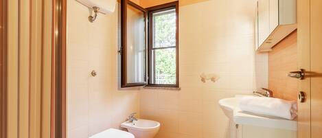 A bathroom with a toilet, bidet, and sink, a window, and wooden ceiling beams.