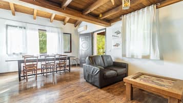 Una habitación con suelo de madera, un sofá de cuero, una mesa de comedor con sillas y un banco de madera.