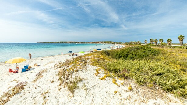 A beach with white sand, clear blue water, and a few umbrellas.