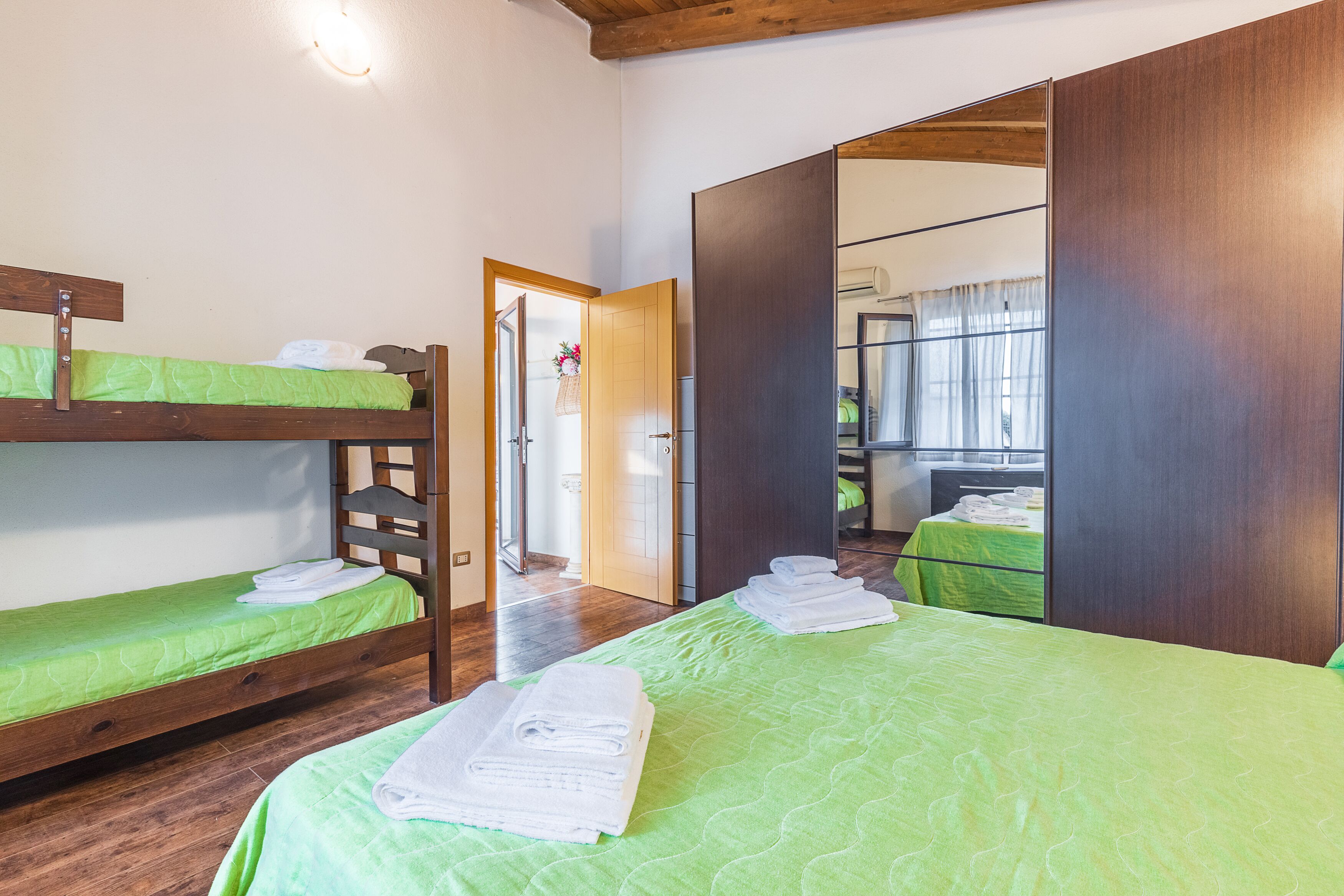 A room with bunk beds and a large mirror. There is a door leading to another room.