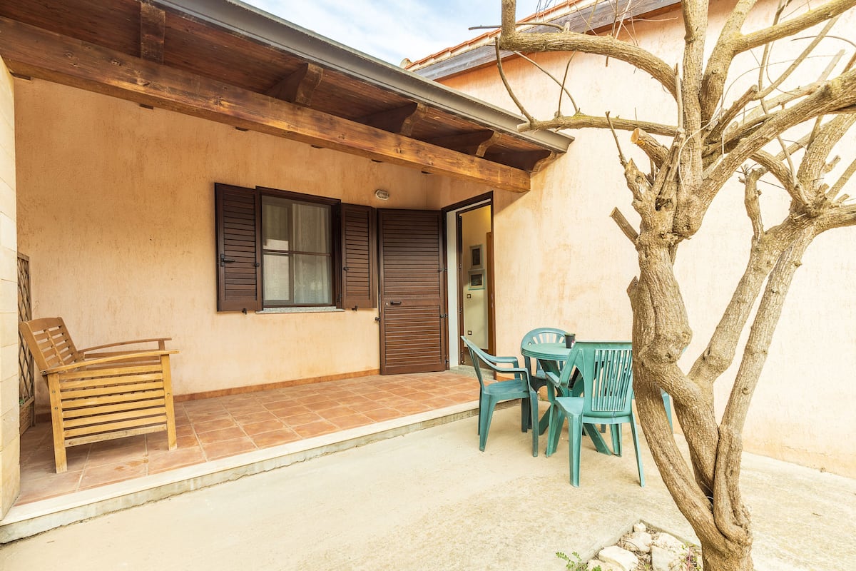 A building with a wooden bench and two chairs outside.