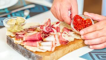 A person arranging a charcuterie board with various meats and a small bowl of olives.