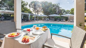 A poolside breakfast setup with a table, chairs, and umbrellas.