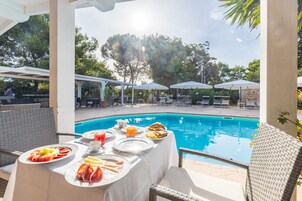 Desayuno junto a la piscina con una mesa, sillas y sombrillas.