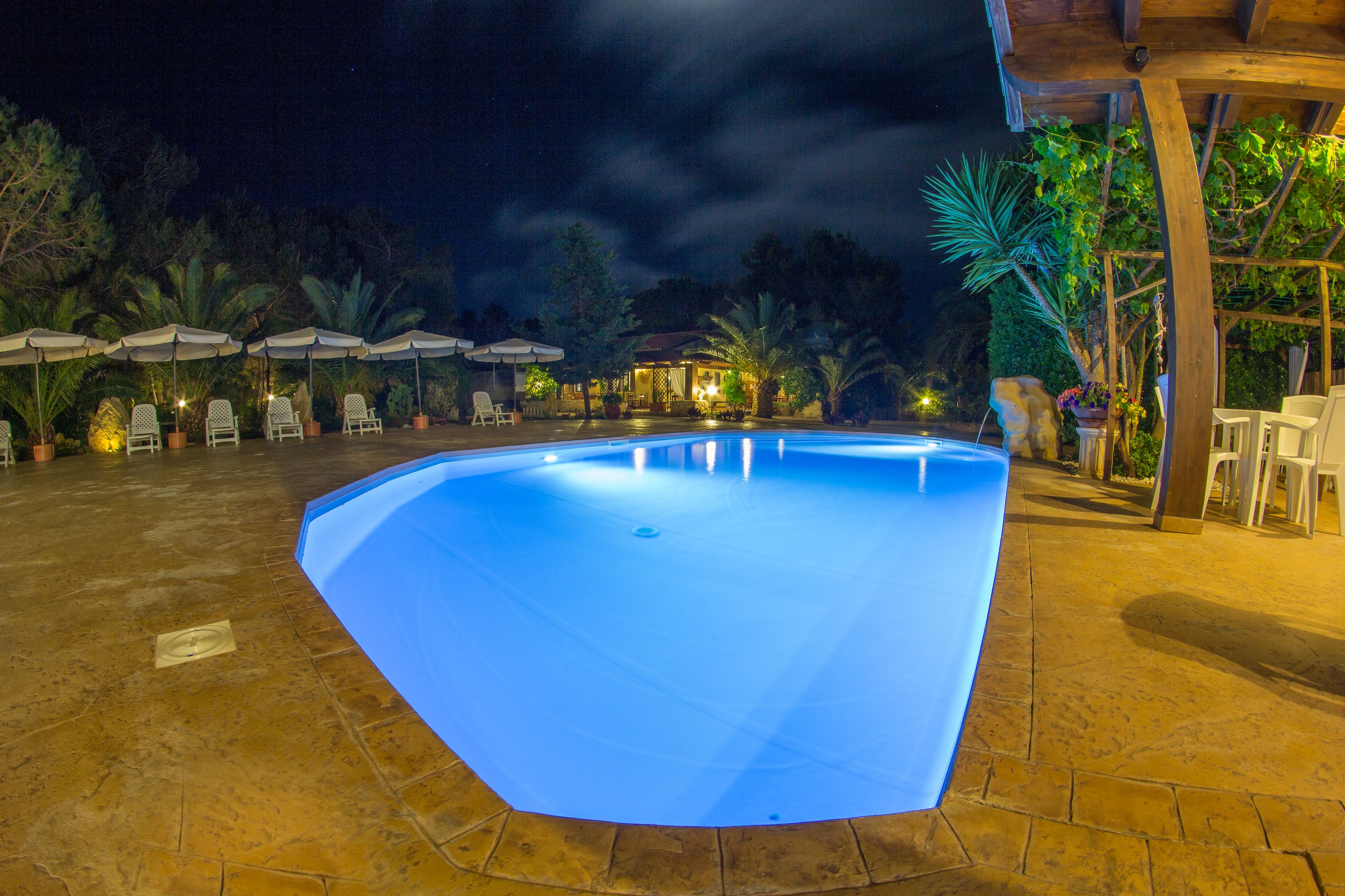 A swimming pool with a curved edge, surrounded by lounge chairs and umbrellas, and a covered area with wooden beams.