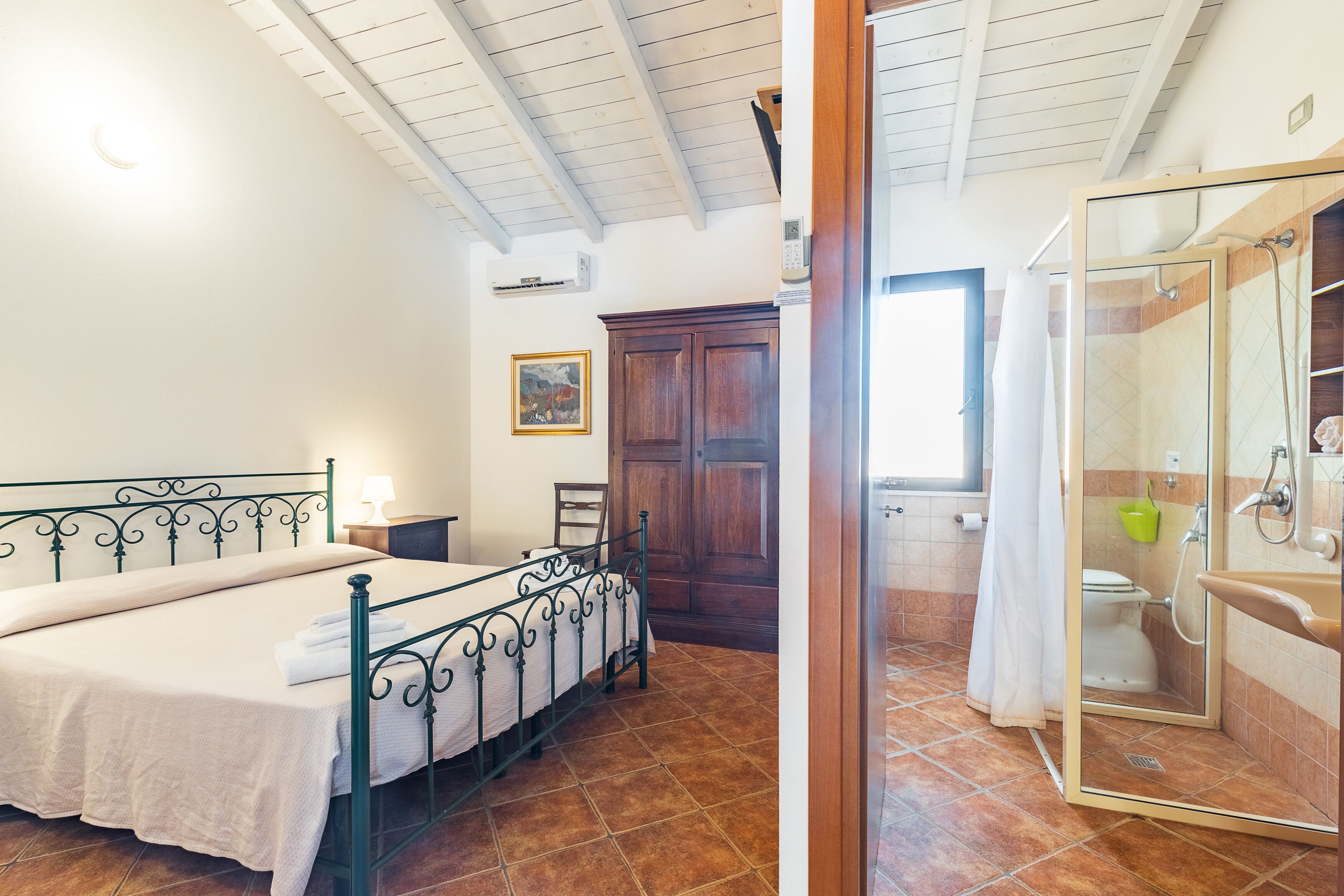 Une chambre à coucher comprenant un lit, une table de chevet, une armoire en bois et une salle de bain avec douche.