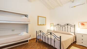 Un dormitorio con una cama litera, una cama individual, una mesita de noche con una lámpara, un mueble auxiliar y un aire acondicionado instalado en la pared.