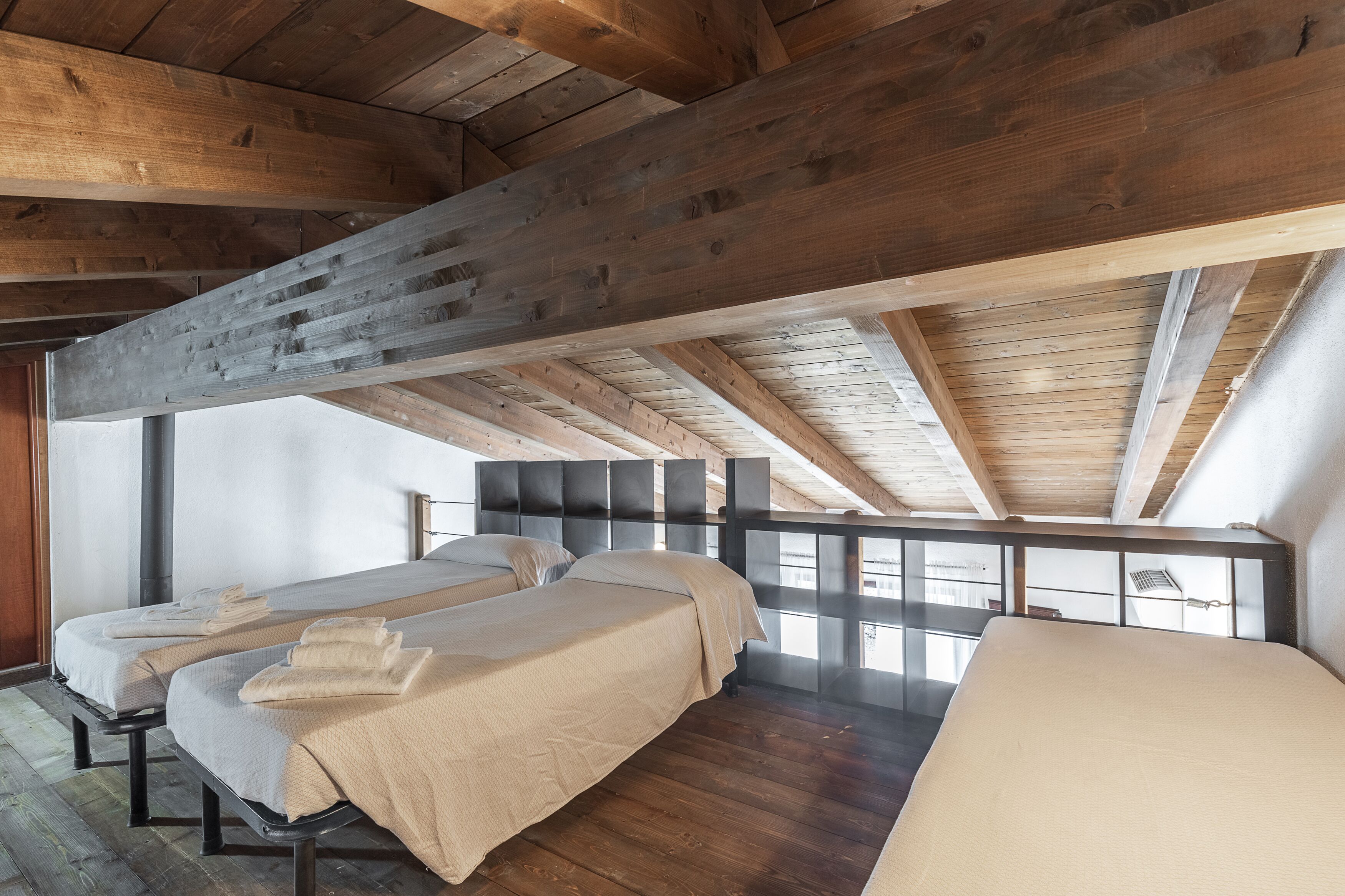 Una habitación con tres camas, vigas de madera y vistas a través de un panel de vidrio.