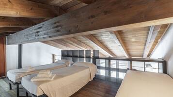 Una habitación con tres camas, vigas de madera y vistas a través de un panel de vidrio.