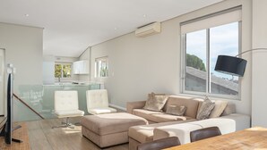 A modern living room with a wooden dining table, beige sofas, and a glass kitchen area. - High Level 1 (Cape Town)
