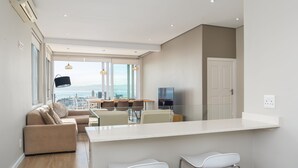 A modern kitchen with a large island, a dining area with a view, and a living space with a sofa and chairs. - High Level 1 (Cape Town)