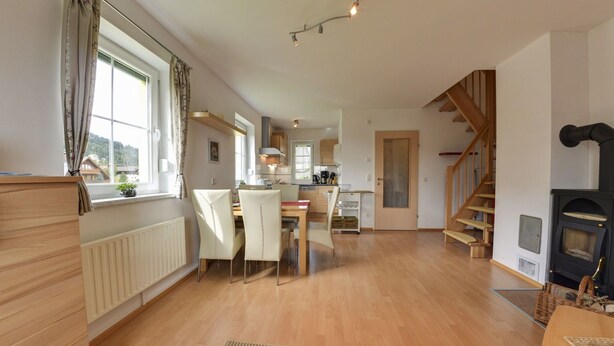 Amplia sala de estar con piso de madera, una mesa de comedor con sillas, zona de cocina y una escalera que lleva a otro nivel.