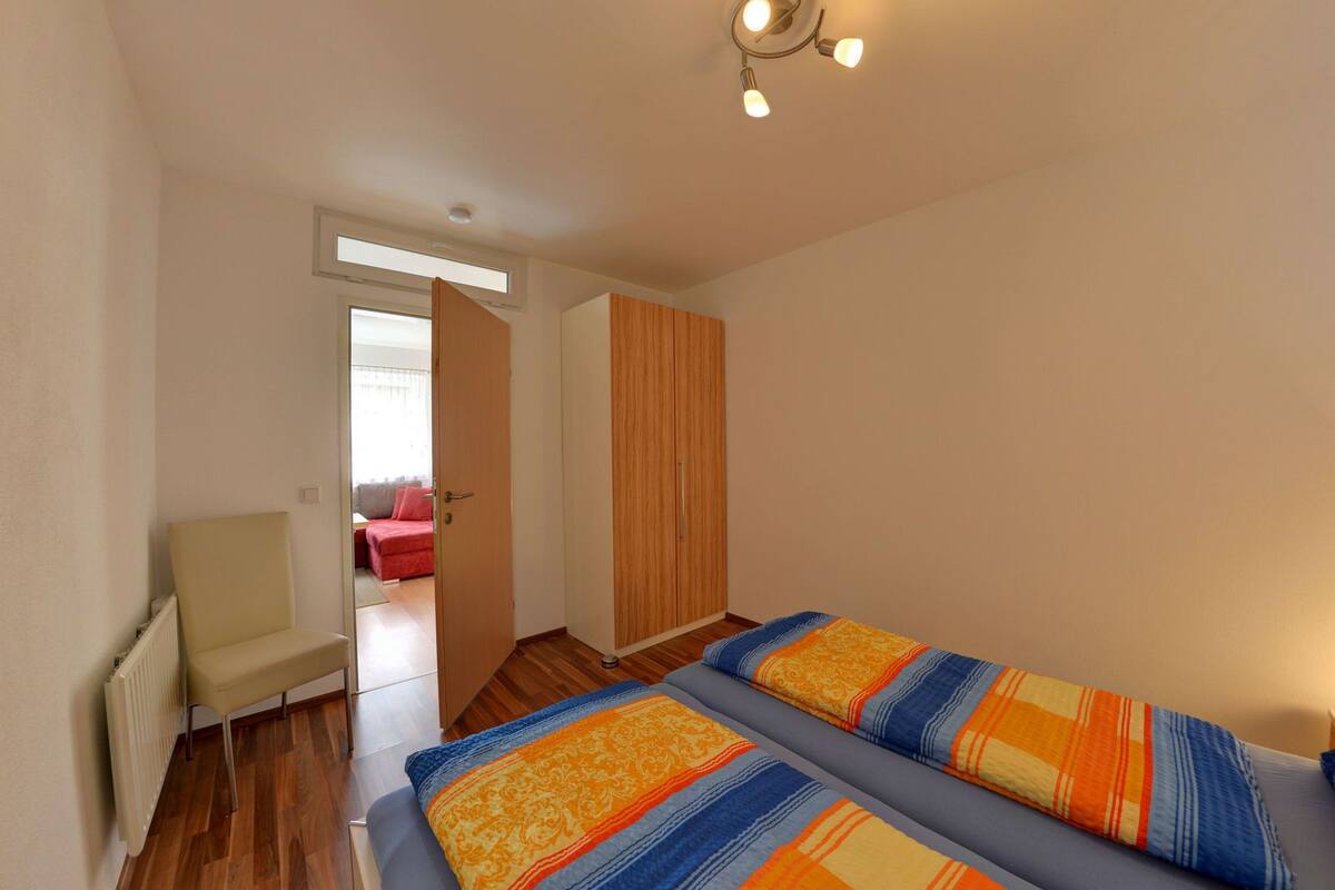 Een slaapkamer met een bed, een stoel, een kledingkast en een deur naar een andere kamer.