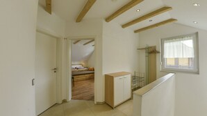 Un pasillo estrecho con techo de madera y una puerta que da a un dormitorio con cama y un pequeño armario.