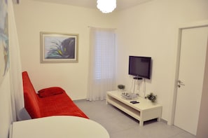 Uma sala de estar moderna com um sofá vermelho, uma mesa de centro branca, uma TV de tela plana e um quadro abstrato na parede.