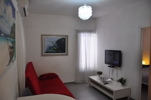 Quarto com sofá vermelho, televisão em móvel, quadro e janela com cortinas.