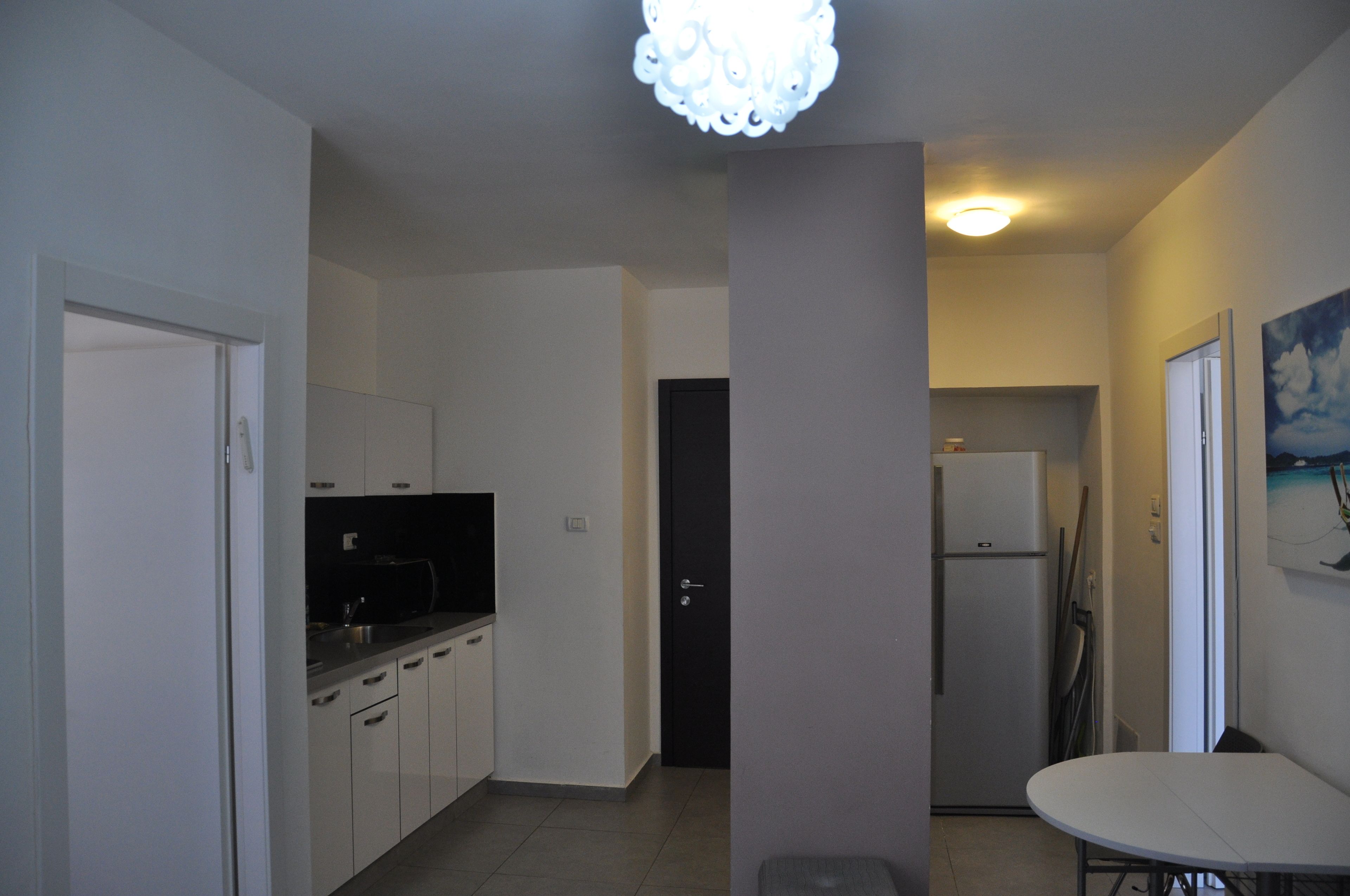 A compact kitchen with white cabinets, a black countertop, and a refrigerator.