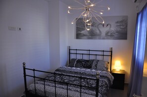 A neatly made bed with patterned bedding, a wall-mounted painting of swans, and a bedside lamp. - Isra Home Rothschild 8-3 Apartment (Bat Yam)