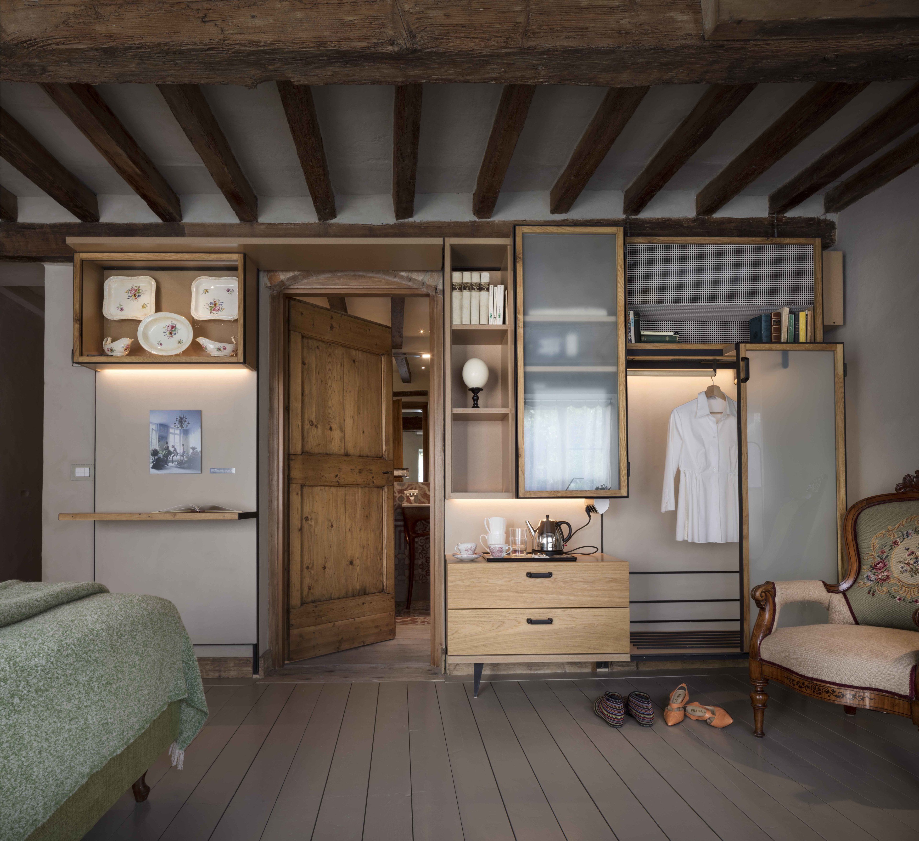 Ein gemütliches Schlafzimmer mit freiliegenden Holzbalken, einem Holzschrank, einem Nachttisch mit Lampe und einem Stuhl mit Blumenmuster.