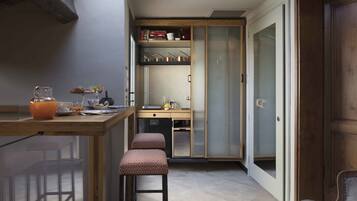 Een compacte keuken met een houten aanrecht, een ingebouwde kookplaat en een koelkast. Er is een eethoek met een houten tafel en twee barkrukken.