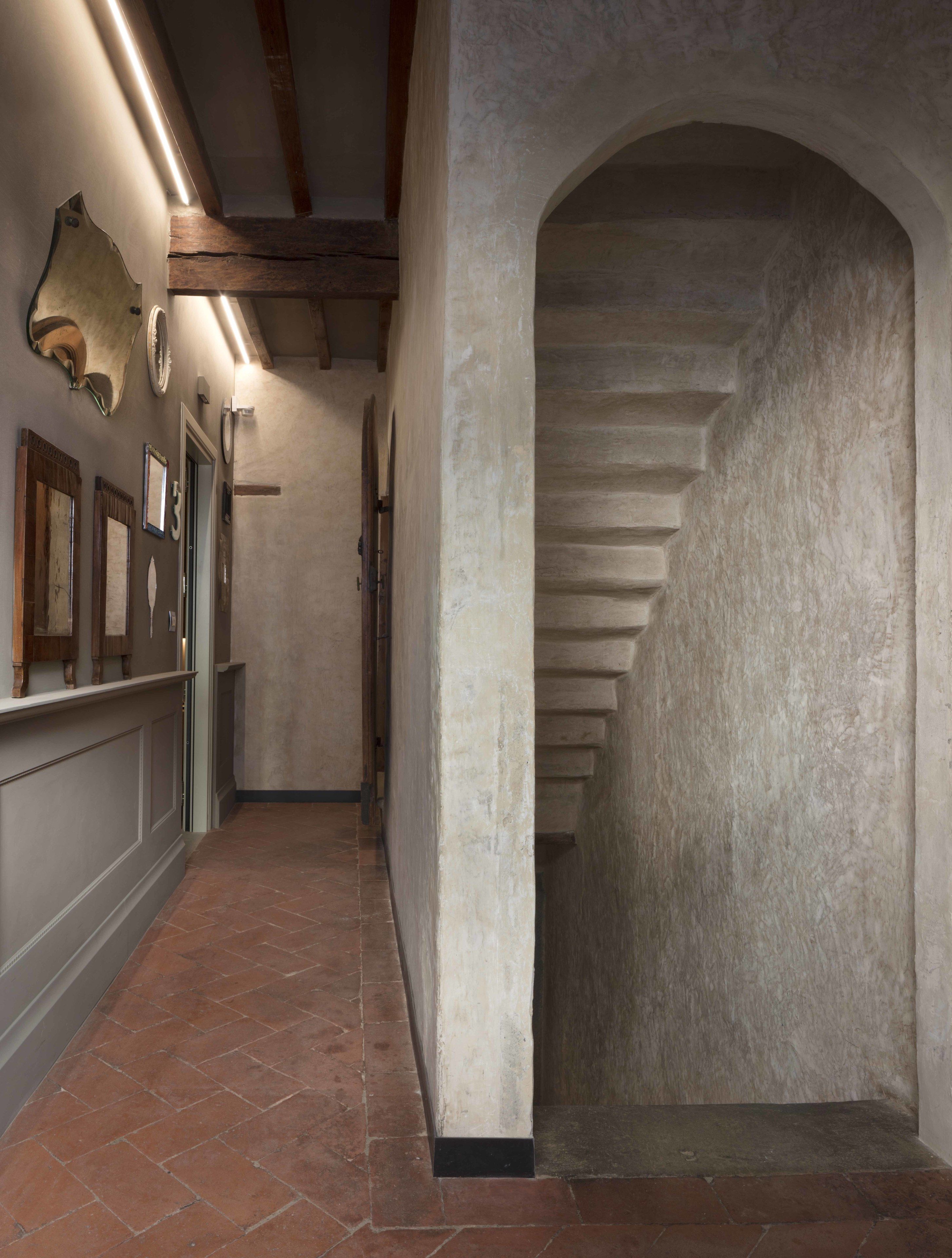 A hallway with a tiled floor, a stone archway, and a series of framed pictures on the wall.