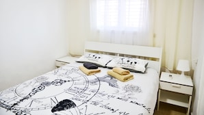 A neatly made bed with a white headboard, two bedside tables, and a window with sheer curtains. - Isra Home Apartment Jabotinsky 8 (Bat Yam)