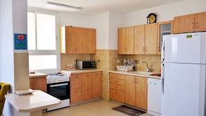 A kitchen with wooden cabinets, a white refrigerator, a microwave, a stove, and a sink. - Isra Home Apartment Jabotinsky 8 (Bat Yam)