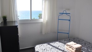 A bedroom with a bed, a window with a view of the sea, a blue hanger, and a small plant on a dresser. - Isra Home Apartments Ben Gurion 81 (Bat Yam)