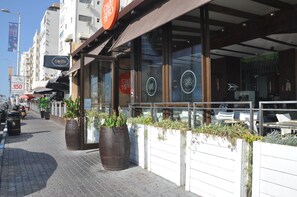 A cafe with outdoor seating, large windows, and potted plants.