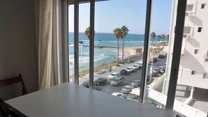 A room with a large window overlooking a beach with palm trees and parked cars. - Isra Home Apartments Ben Gurion 81 (Bat Yam)