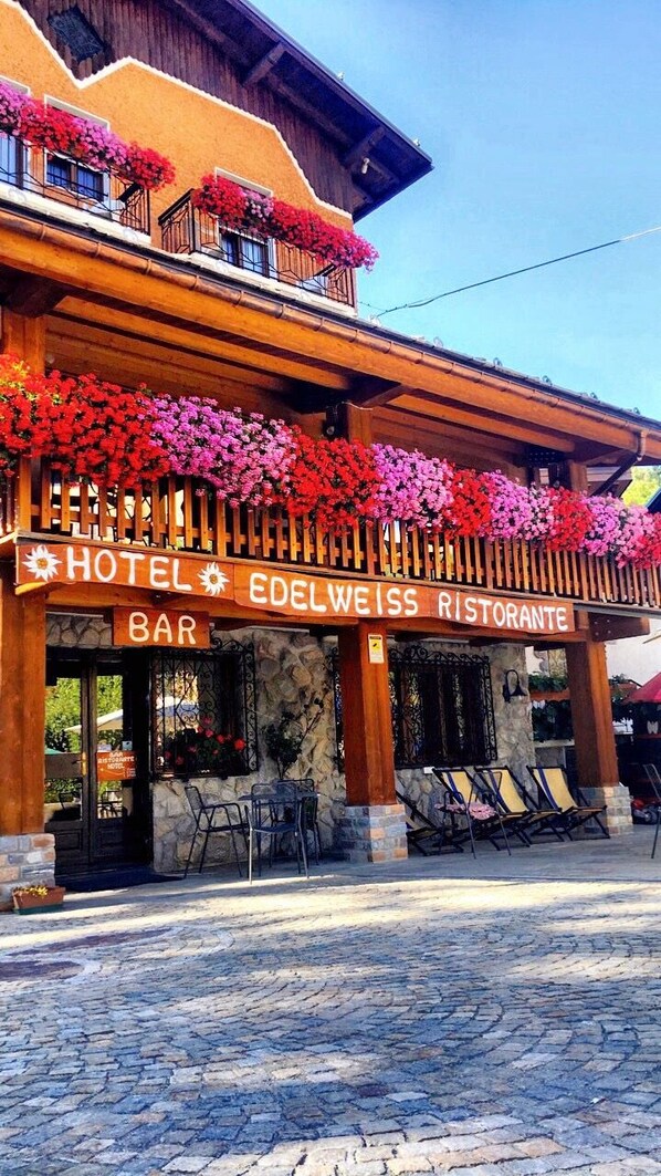 Un bar de hotel con fachada de madera, mesas al aire libre y macetas con flores.