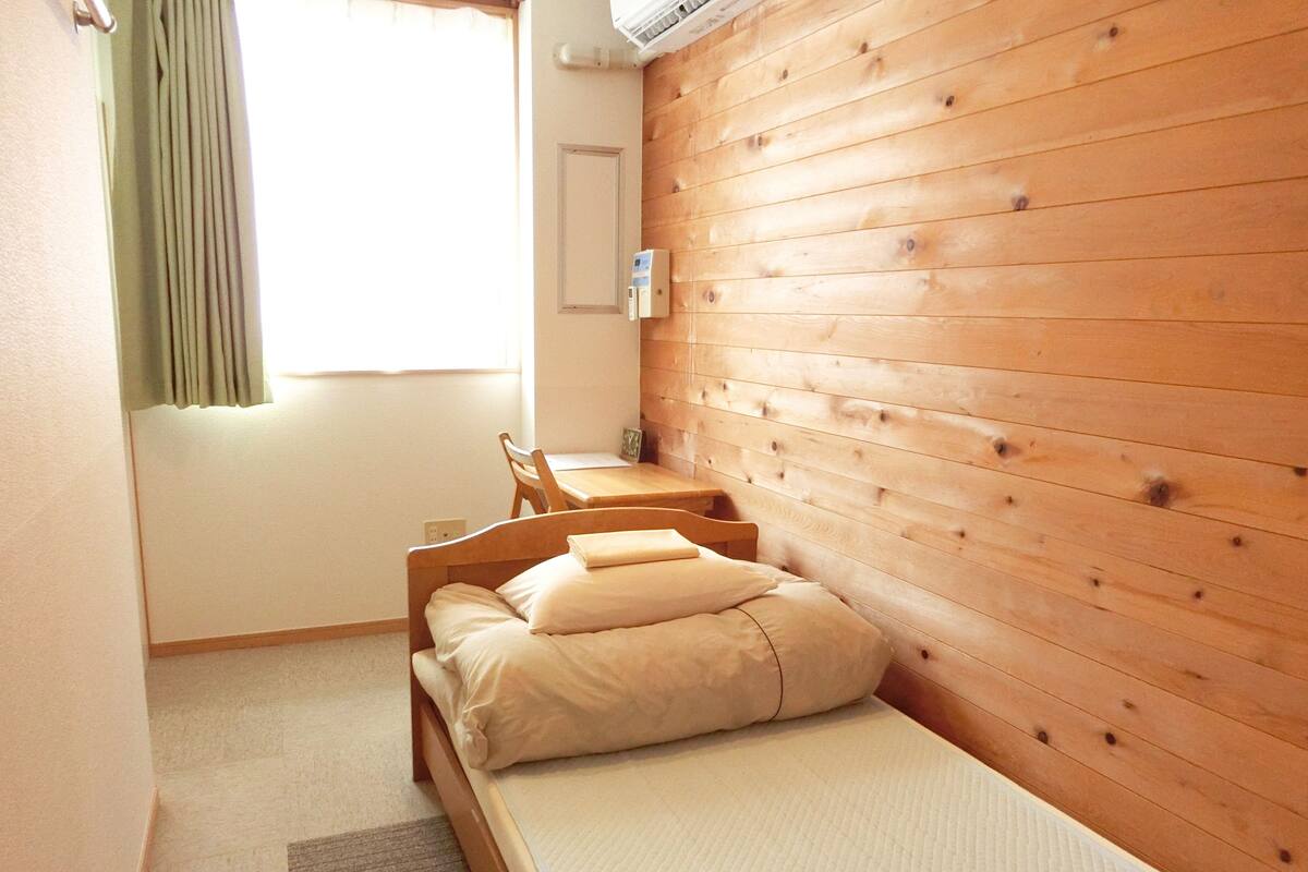 Una habitación pequeña y acogedora con cabecera de madera, una cama individual con almohadas, un escritorio de madera y una silla.
